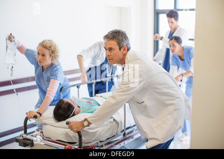 I medici e gli infermieri correre il paziente sulla barella verso il basso corridoio ospedale Foto Stock