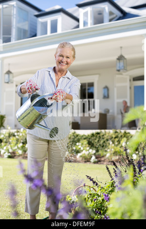 Ritratto di sorridere senior donna fiori di irrigazione in giardino Foto Stock