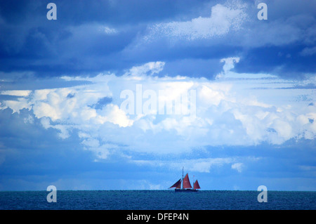 Red vele della nave su orizzonte con tempestoso cielo velato Foto Stock