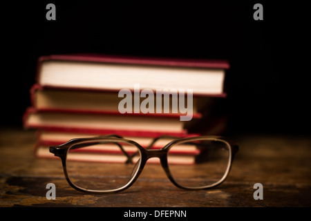 Paio di Occhiali sulla superficie di legno con la pila di libri in background Foto Stock