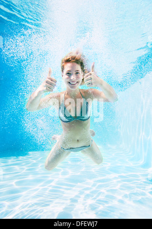 Donna che Thumbs up sott'acqua in piscina Foto Stock