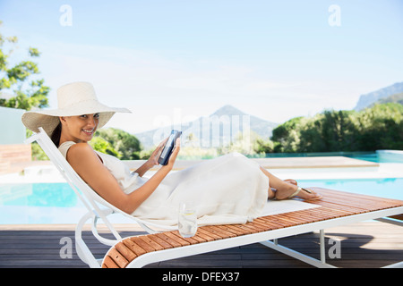 Donna con tavoletta digitale sulla sedia a sdraio a bordo piscina Foto Stock