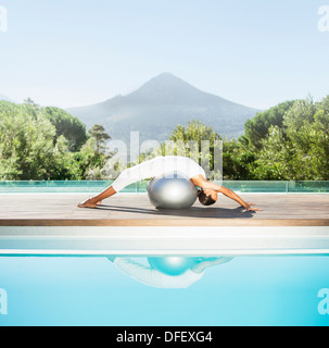 Donna stretching over sfera fitness a bordo piscina Foto Stock