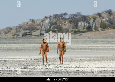 San bushman trackers attraversando a piedi il incrinato pan lontano dalle antiche affioramento di granito di Kubu Island (Lekhubu), Makgadikgadi Pan, Botswana Foto Stock