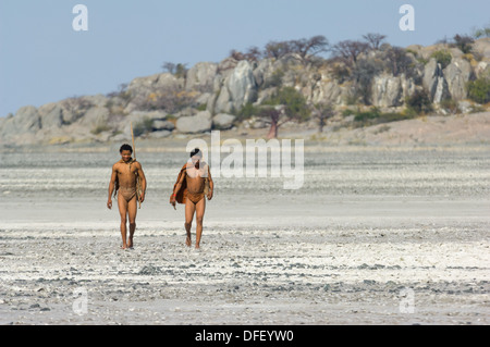 San bushman trackers attraversando a piedi il incrinato pan lontano dalle antiche affioramento di granito di Kubu Island (Lekhubu), Makgadikgadi Pan, Botswana Foto Stock