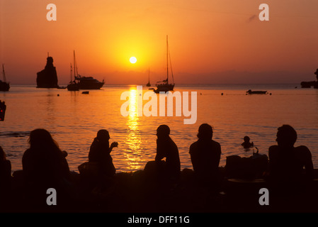 I turisti a guardare il tramonto off Spiaggia Benirras, Ibiza, Isole Baleari, Spagna Foto Stock