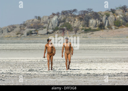 San bushman trackers attraversando a piedi il incrinato pan lontano dalle antiche affioramento di granito di Kubu Island (Lekhubu), Makgadikgadi Pan, Botswana Foto Stock