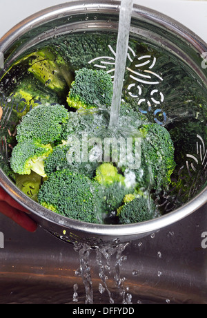 Broccoli di risciacquo in un colapasta sotto l'acqua corrente. Foto Stock