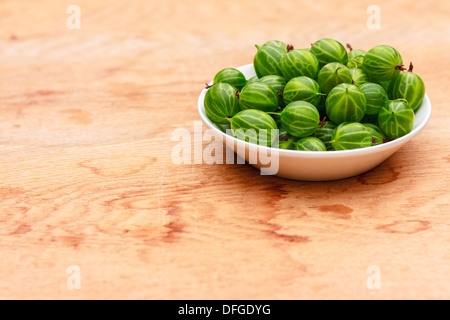 Piatto bianco riempito con piante succulente succosa fresche e mature Ribes verde su un vecchio tavolo di legno alto. Foto Stock