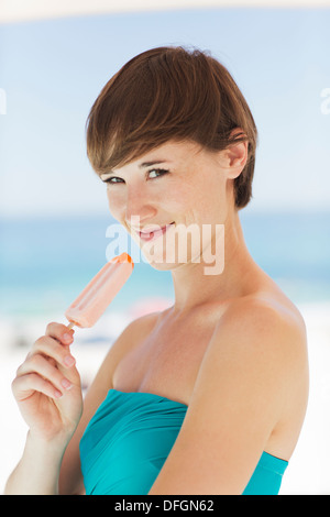 Donna di mangiare ghiaccio aromatizzato sulla spiaggia Foto Stock