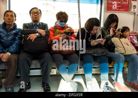 I passeggeri che utilizzano i telefoni cellulari sul treno della metropolitana, Seoul, Corea Foto Stock