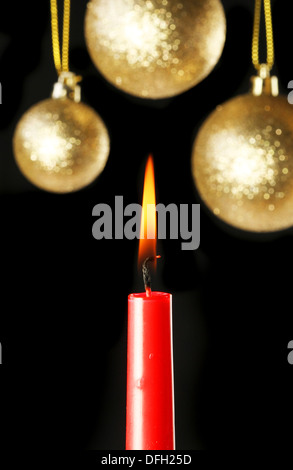 Tema Natale, bruciando candela rossa contro uno sfondo di oro baubles in soft focus Foto Stock