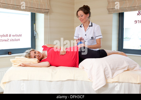 Un sorridente donna incinta ricevere un massaggio da un fisioterapista presso un centro termale olistico per la gravidanza. Foto Stock
