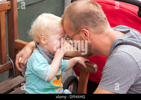 Il pianto del bambino di essere confortati e tranquillizzati dal suo padre. Foto Stock