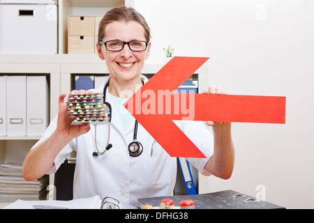 Felice medico donna rivolta freccia rossa a medici pillole nel suo ufficio Foto Stock