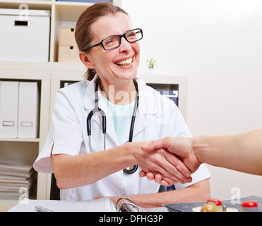 Felice femmina senior medico handshake dando ad un paziente nel suo ufficio Foto Stock