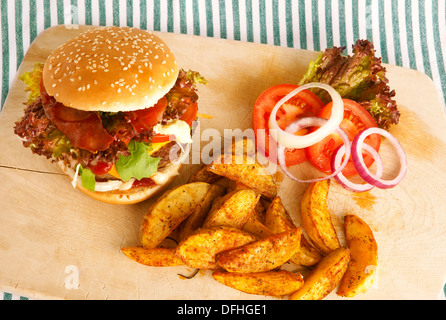 Burger con spicchi di patate a bordo; verde e bianca a strisce tovaglia, pomodori come decorazione Foto Stock