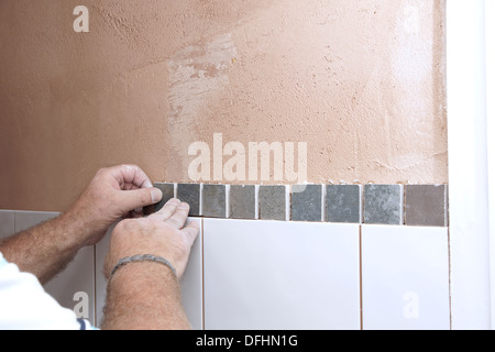 Installatore di attaccare le piastrelle in una camera umida / doccia / bagno su un nuovo muro intonacato Foto Stock