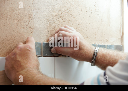 Installatore di attaccare le piastrelle in una camera umida / doccia / bagno su un nuovo muro intonacato Foto Stock