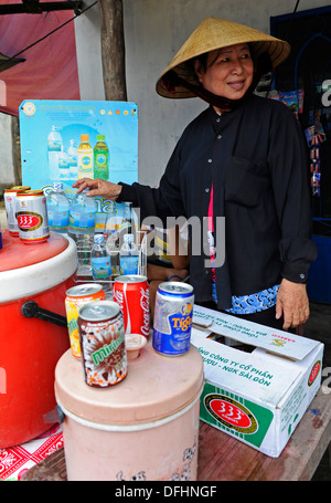 Donna vietnamita la vendita di conserve di birra e bevande indossando un tradizionale cappello conico. Foto Stock