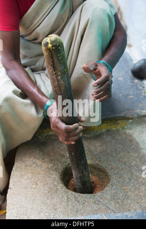 Donna indiana usando un mortaio e un pestello per macinare spezie al di fuori del suo villaggio rurale casa. Andhra Pradesh, India Foto Stock