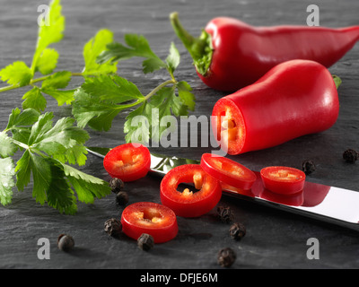 Di peperoncino rosso fresco intero e tagliato con foglie di coriandolo fresco. Foto Stock