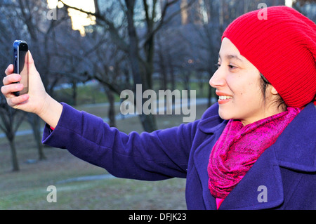 Bella donna Latino utilizzando smart phone nel Central Park di New York City, Stati Uniti d'America Foto Stock