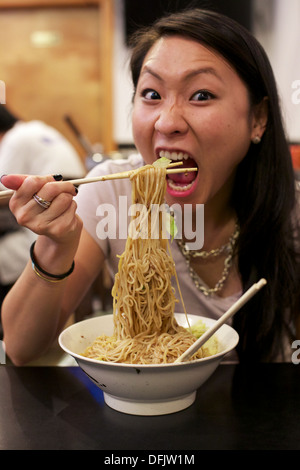 Giovane ragazza asiatica di mangiare a base di noodle cinesi piatto in un ristorante a Chinatown Manhattan, New York, NY, STATI UNITI D'AMERICA. Foto Stock