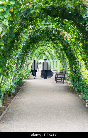 Due donne musulmane camminare in un tunnel di edera in Kensington Palace, London, Regno Unito Foto Stock