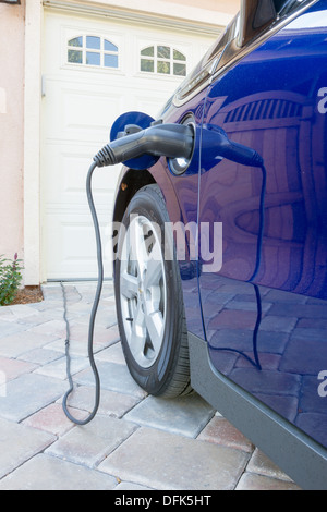 Ibridi Plug-in auto con il connettore collegato e Ricarica parcheggiato a casa in un viale di accesso Foto Stock