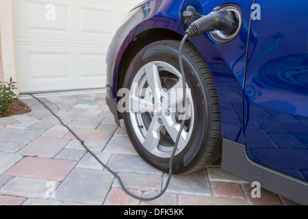 Ibridi Plug-in auto con il connettore collegato alla presa di corrente e caricare a casa in un viale di accesso Foto Stock