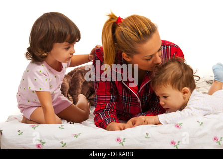 Madre con i suoi bambini sdraiato sul letto e mom kissing piccola testa di bambino Foto Stock