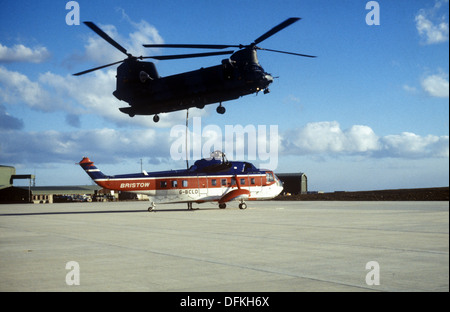 Un RAF Boeing elicottero Chinook sollevamento di un danneggiato Bristow Sikorsky S-61 elicottero nelle isole Falkland Foto Stock