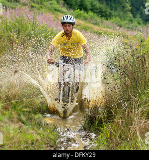 Un giovane uomo su una mountain bike attraverso una pozza di fango nel paesaggio erboso Foto Stock