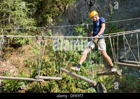 Giovane uomo attraversando il ponte di albero, vincendo la sua paura delle altezze Foto Stock