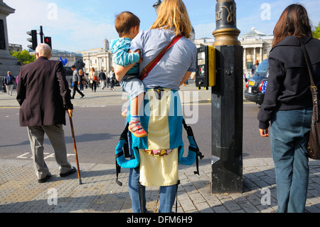 Londra, Inghilterra, Regno Unito. Trafalgar Square - donna che porta il suo figlio, in attesa di attraversare la strada Foto Stock