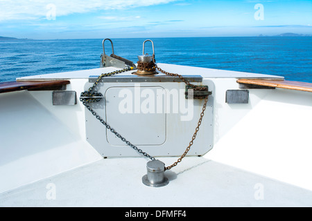 La prua di un passeggero con una barca di crociera mostra la sua rusty catena di ancoraggio, bitte e verricello tra un cielo blu e isole distanti. Foto Stock