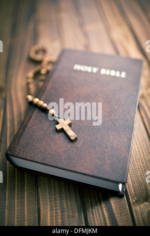 La Santa Bibbia con i grani del rosario su sfondo di legno Foto Stock