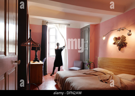 Donna apertura tende, camera da letto con letto doppio, B e B chambre avec vue, Luberon, Francia Foto Stock