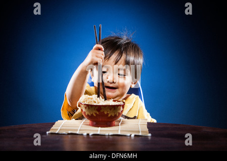 Una bambina di 16 mesi, Japanese-American boy, mangia spaghetti ramen con bacchette su un bambù matt. Foto Stock