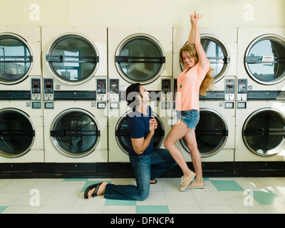Una smart giovane uomo si mette in ginocchio davanti a una bella donna di San Diego lavanderia a gettone. Foto Stock