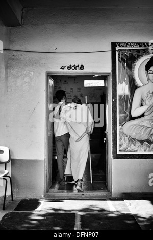 Vecchio sadhu indiano essendo aiutato nello Sri Sathya Sai Baba outreach mobile hospital Clinic. Andhra Pradesh, India. Monocromatico Foto Stock