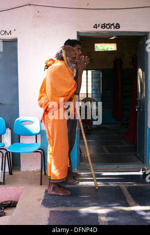 Vecchio sadhu indiano essendo aiutato nello Sri Sathya Sai Baba outreach mobile hospital Clinic. Andhra Pradesh, India Foto Stock