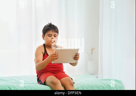 Ragazzo seduto sul letto e utilizzando una tavoletta digitale Foto Stock