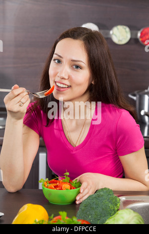 Bella e giovane donna mangia insalata in cucina domestica Foto Stock