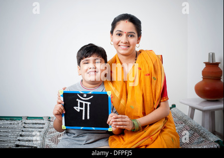 Ritratto di una donna seduta con suo figlio tenendo un ardesia con parola Maa scritto su di esso Foto Stock