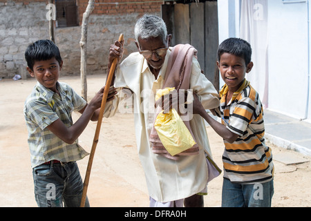 Due ragazzi indiani aiutando un vecchio uomo indiano con il bastone da passeggio a Sri Sathya Sai Baba mobile ospedale outreach. India Foto Stock