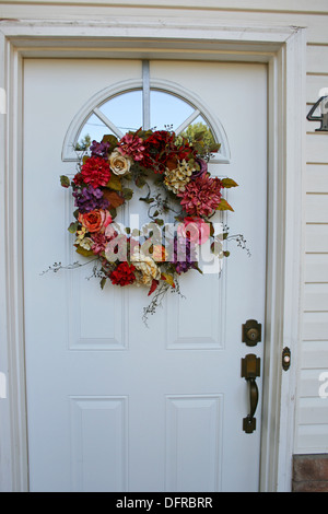 Colorata ghirlanda floreale appeso sulla porta bianca della casa Foto Stock