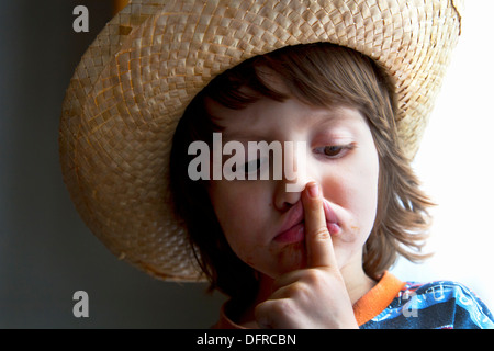 Quattro e una metà anno vecchio ragazzo che indossa un cappello di vimini tenendo il suo dito indice per la sua bocca. Foto Stock