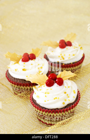 Tortini di cioccolato con glassa alla vaniglia e rosso caramella Holly bacche e oro foglie fondente Foto Stock